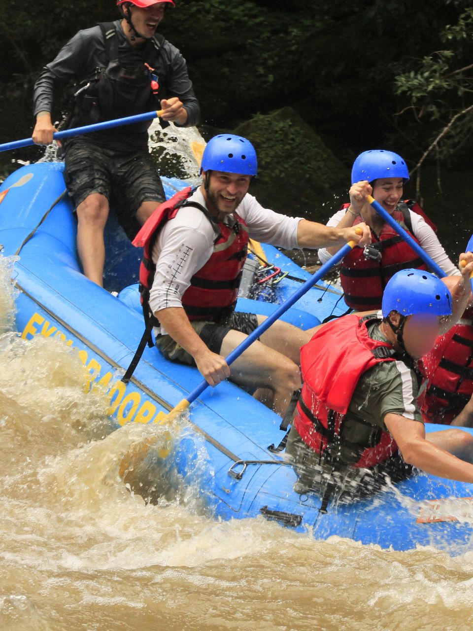 Matze and Becca of Oso Osito in a raft on a white water rafting tour (arguably the best thing to do in Puerto Viejo and the surrounding area!!) - wearing helmets, life vests, and giant smiles. Holding oars and trying to keep the raft afloat with the guide shouting int he back. 