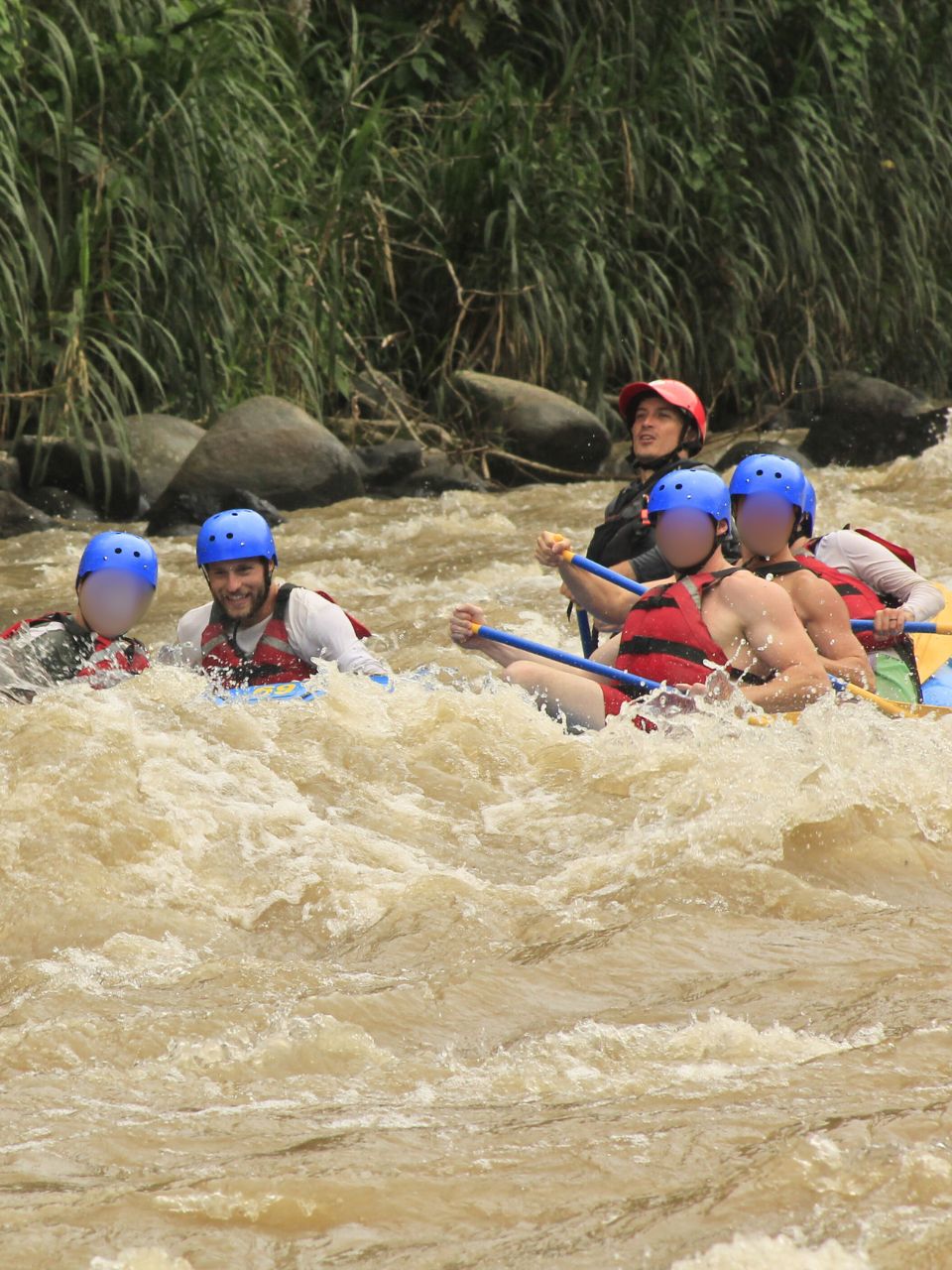 Matze and Becca of Oso Osito in a raft on a white water rafting tour (arguably the best thing to do in Puerto Viejo and the surrounding area!!) - wearing helmets, life vests, and giant smiles. Due to the angle, the raft is almost invisible behind the waves and muddy water and so it looks almost like the entire group is sitting directly in the river! 