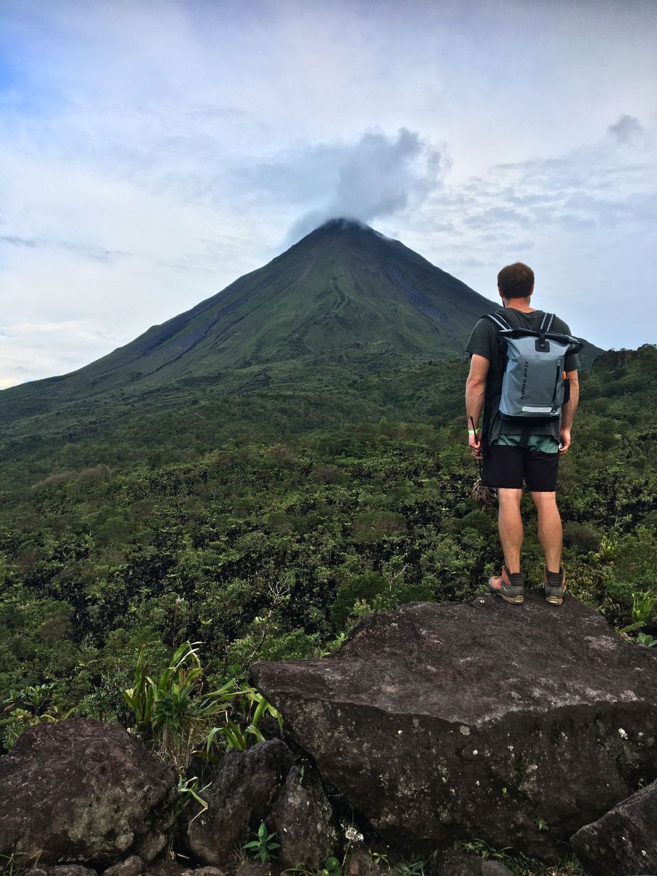Matthias of Oso Osito standing on a black volcanic rock overlooking a valley at the base of Arenal Volcano. During a day tour which is easily one of the best things to do in La Fortuna!