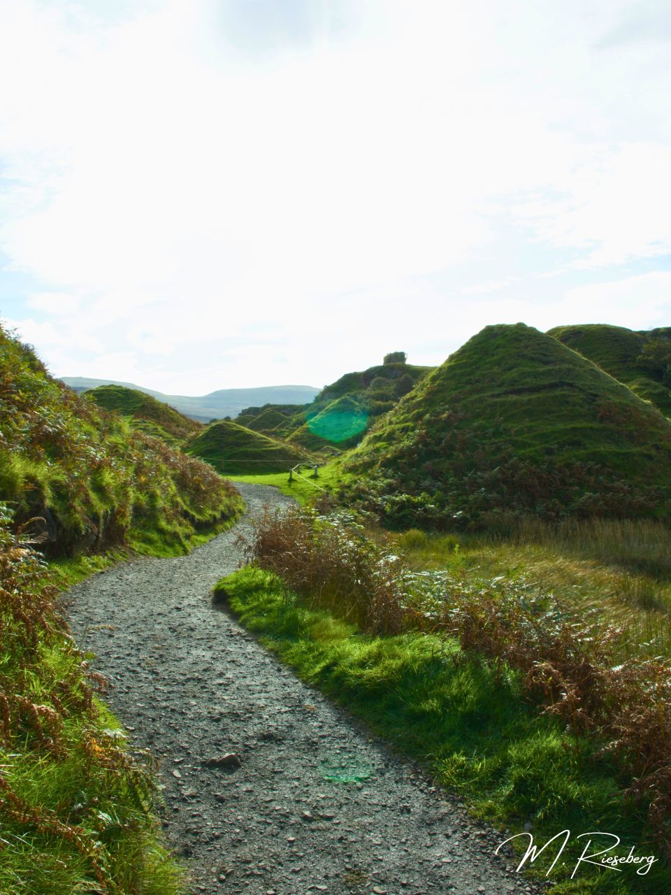The Fairy Glen in Isle of Skye, Scotland, with its wavy, little hills. They are no more than 10-20 feet tall and have layers of wavy patters on them, covered in bright green grass. You can see a handful in this image and they fade into the background where there are even more!