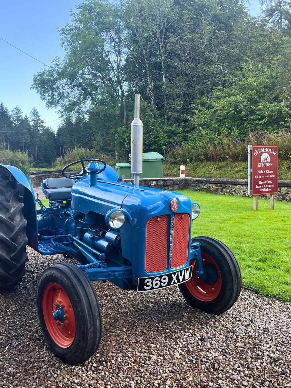 picture of a blue tractor with red wheels and a red grill on a gravel path next to a bit of grass and a sign about farmhouse kitchen breakfasts in Scotland
