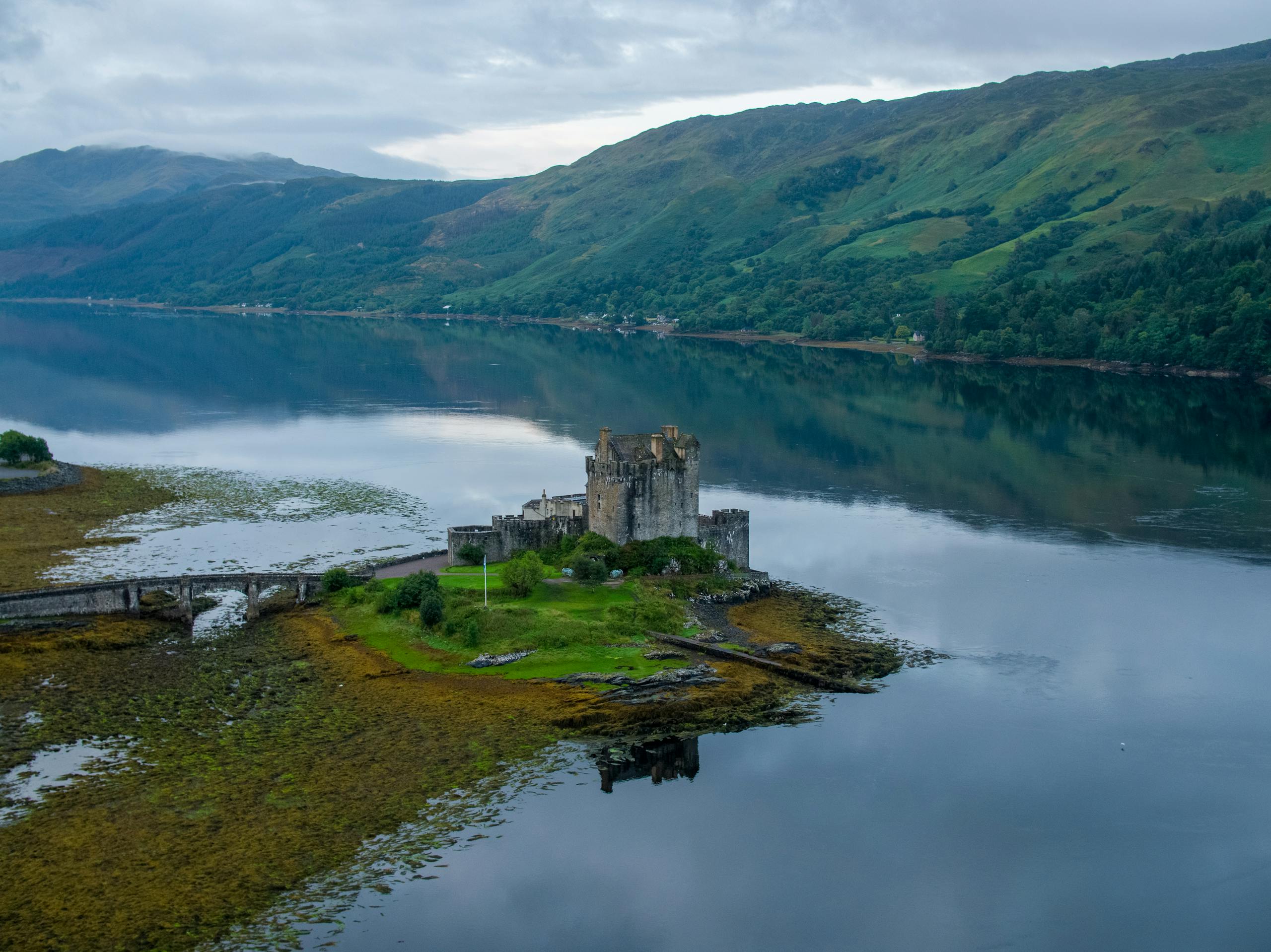 Stunning aerial shot of Eilean Donan Castle surrounded by tranquil waters and lush hills in Scotland.